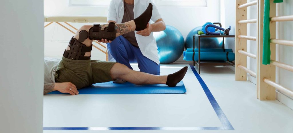 Young physiotherapist exercises in a bright medical office with his injured patient